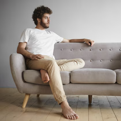isolated view thoughtful young man with bare feet sitting indoors sofa