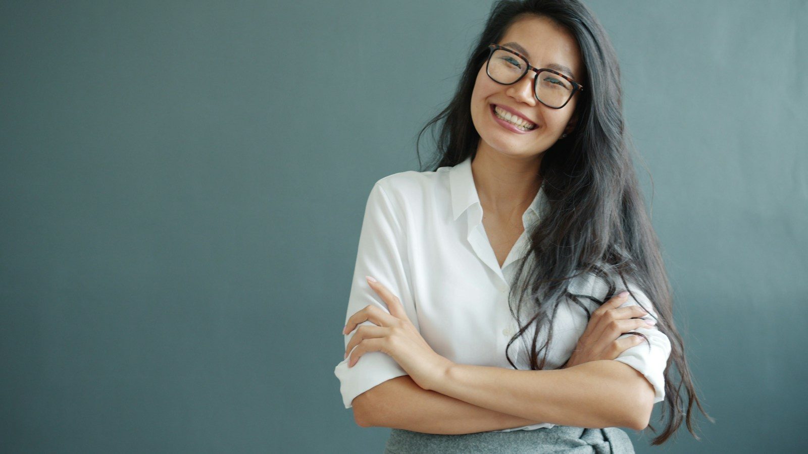 A smiling woman with glasses and arms crossed